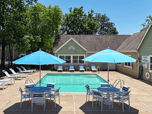 A pool surrounded by chairs and umbrellas with a house in the background.