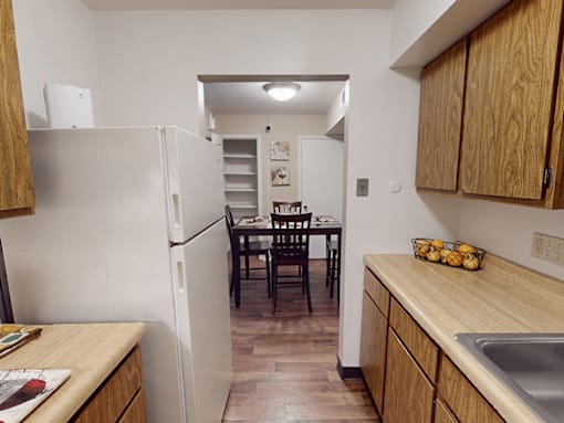 A kitchen with a white refrigerator, wooden cabinets, and a dining table with chairs.