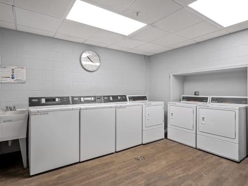 a laundry room with white washers and dryers and a clock on the wall