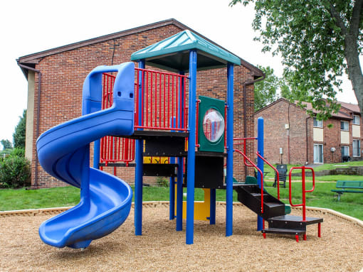 a playground with a blue slide in front of a brick building