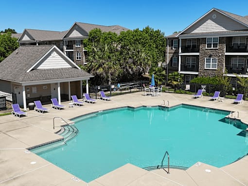 A swimming pool surrounded by lounge chairs and buildings in the background.