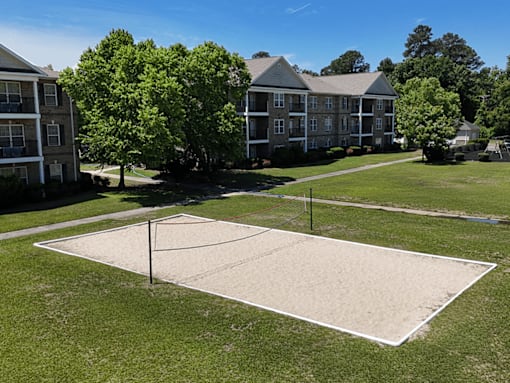 A tennis court is located in a grassy area in front of apartment buildings.