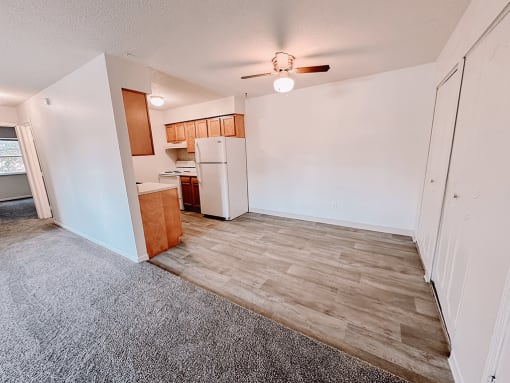 an empty living room with a kitchen and a ceiling fan