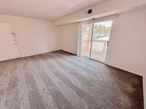 an empty living room with a sliding glass door to a balcony