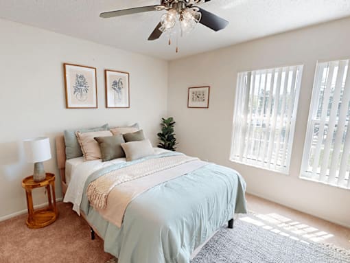 A bedroom with a bed, a ceiling fan, and pictures on the wall.