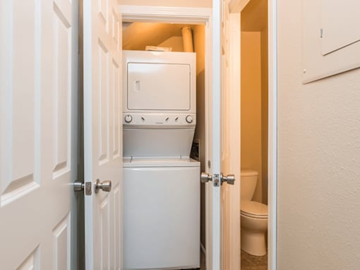 A white door opens to a small bathroom with a toilet and a white cabinet.