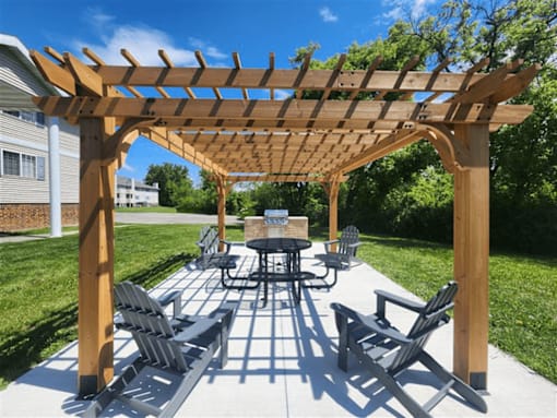 A wooden pavilion with a table and chairs and grill