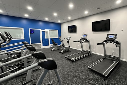 A gym with treadmills, exercise bikes, and a television.