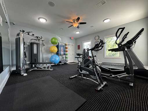 A spacious gym with a variety of equipment including a treadmill, a stationary bike, a rowing machine, a weight machine, and a bench press.