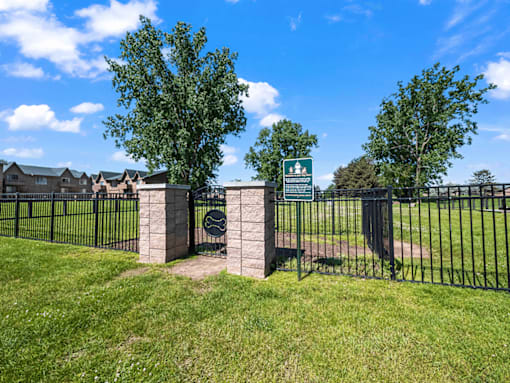 A green sign is on a gate in front of a grassy area.