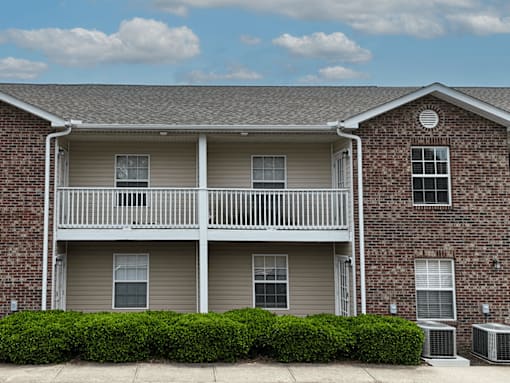 A brick apartment building with a balcony and bushes in front.