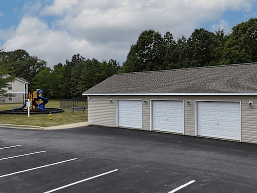 A parking lot with a playground and a building with three garage doors.