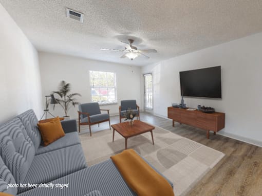 A living room with a grey couch, a wooden coffee table, a flat screen TV, and a ceiling fan.