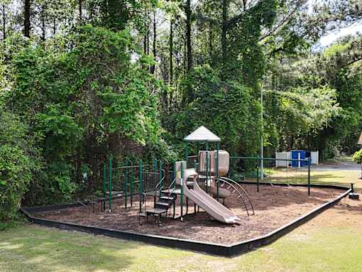A playground with a slide and swings surrounded by trees.