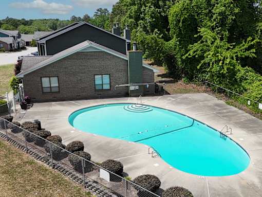 A small house with a green roof is surrounded by a pool and trees.