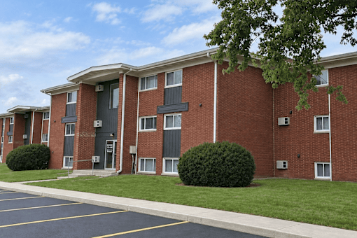 A red brick apartment building with a parking lot in front.
