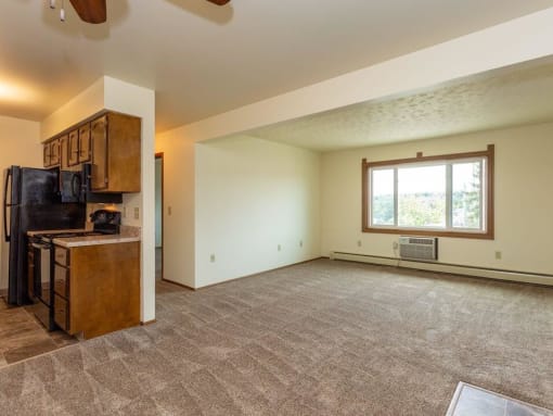 an empty living room with a kitchen and a large window
