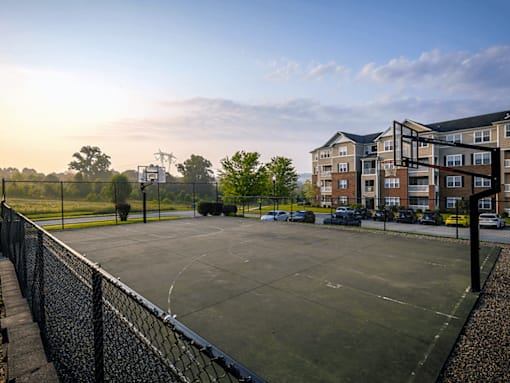 A basketball court is surrounded by a black fence and apartment buildings.
