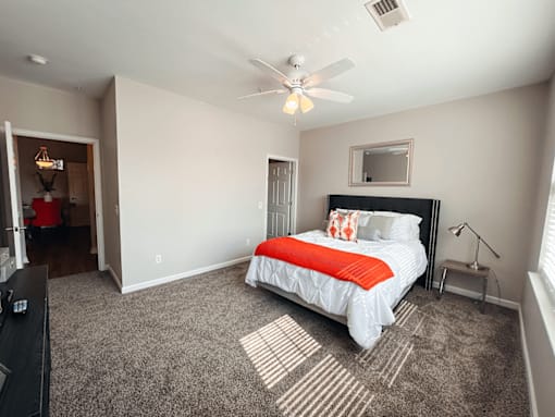 A spacious carpeted bedroom with a bed, a ceiling fan, and attached bathroom.