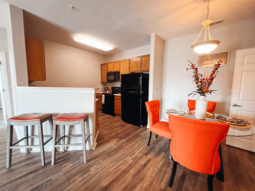A kitchen with a black refrigerator and a dining table with chairs.