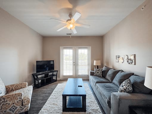 A living room with a grey couch, a coffee table, and a ceiling fan.