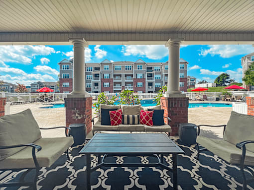 A patio with a table and chairs overlooking a pool and apartment building.