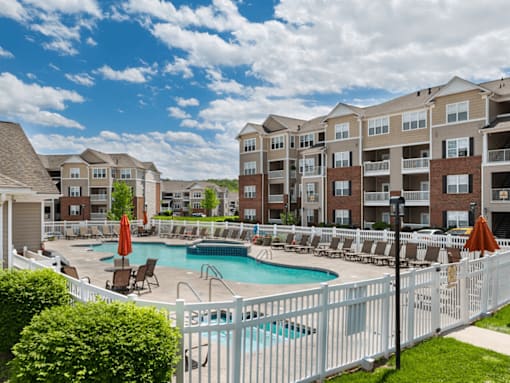 A white fence surrounds a pool in front of apartment buildings.