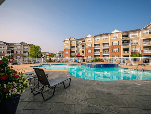 A pool area with a chair and a bench in front of apartment buildings.