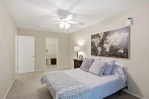 A bedroom with a bed, a ceiling fan, and a painting on the wall.