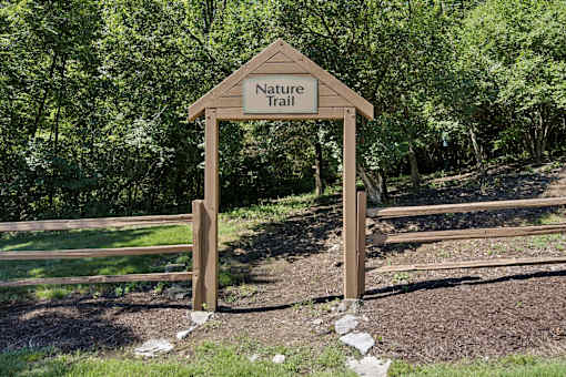 A wooden Nature Trail sign is in front of a wooded area.