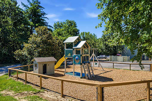 A playground with a yellow slide and a brown wooden fence.
