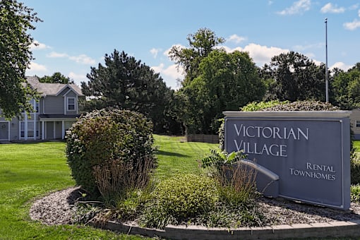 A sign for Victorian Village Rental Townhomes is surrounded by shrubbery.