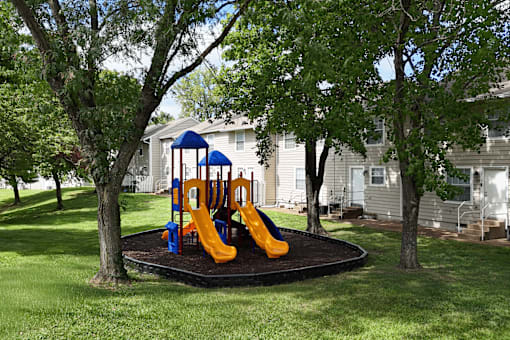 A playground with a blue and yellow slide in the middle of a grassy area.