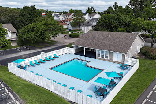A pool surrounded by a white fence with blue umbrellas.