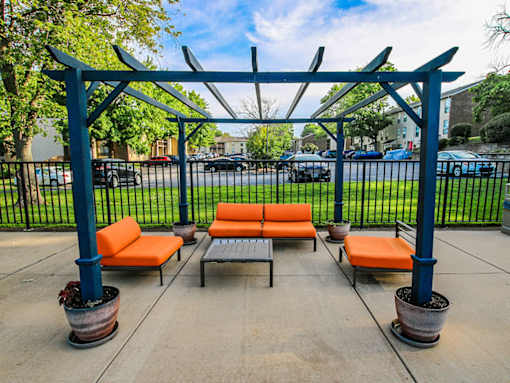 A blue pergola with orange cushions is in the middle of a paved area.