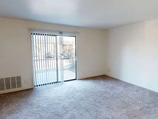 A room with a carpeted floor and a sliding glass door leading to a parking lot.
