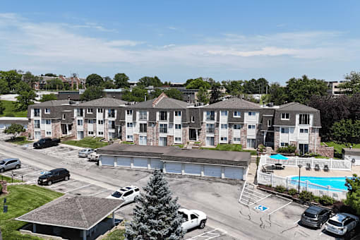 Apartment complex with a pool and cars parked in the parking lot.