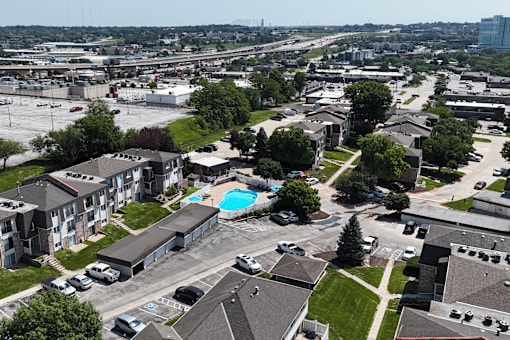 A view of a residential area with apartment buildings, a swimming pool, and cars parked in the parking lot.