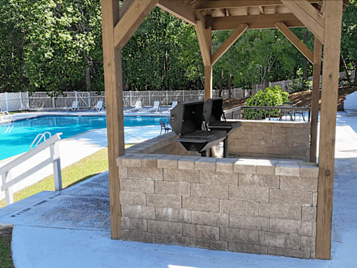 A wooden pergola with a grill is situated next to a pool.