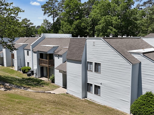 A building with a grey siding and a brown roof is surrounded by greenery.