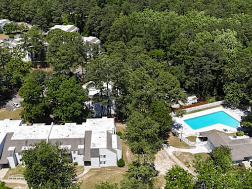 A bird's eye view of a residential area with houses and a swimming pool surrounded by trees.
