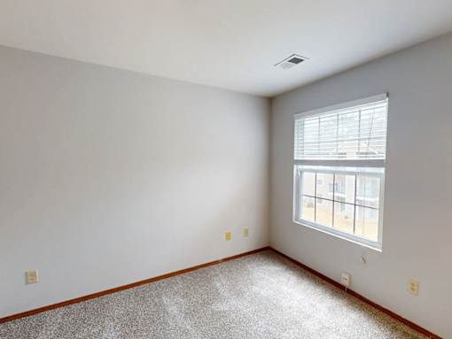 A room with a window and a carpeted floor.