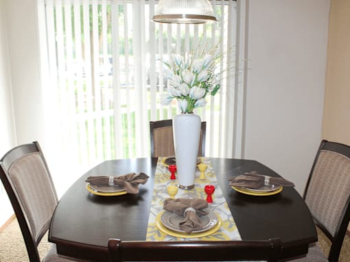 A dining table set with plates and napkins with a vase of flowers in the middle.