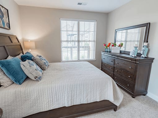 A bedroom with a large bed, a dresser, and a window with blinds.