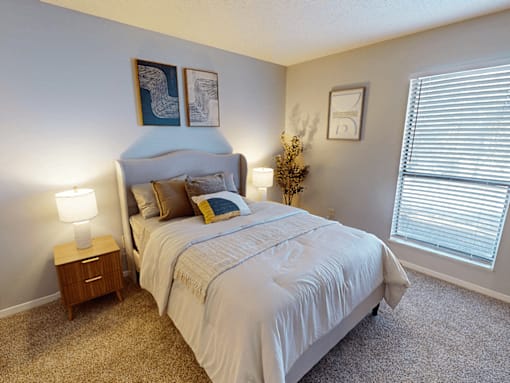 A bedroom with a bed, nightstand, and a small tree.
