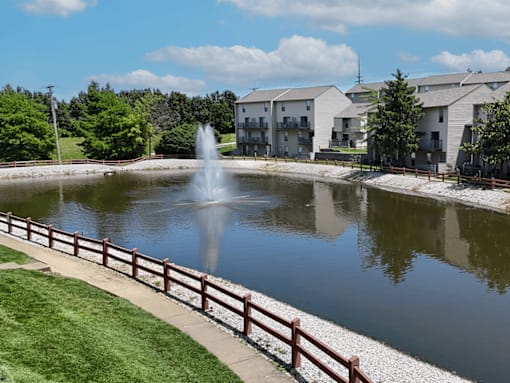 A fountain in the middle of a private lake with a wooden fence around it.