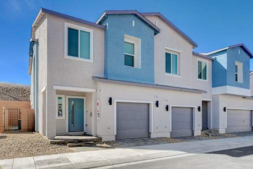 A modern two-story house with a blue door and garage doors.at Copper Creek Apartments, Las Vegas