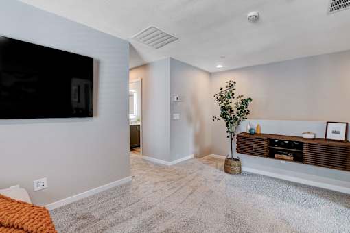 A living room with a grey carpet and a flat screen TV mounted on the wall.at Copper Creek Apartments, Las Vegas