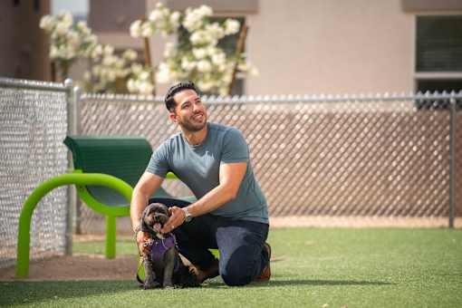 A man kneeling on the ground with his dog.at Copper Creek Apartments, Las Vegas, NV