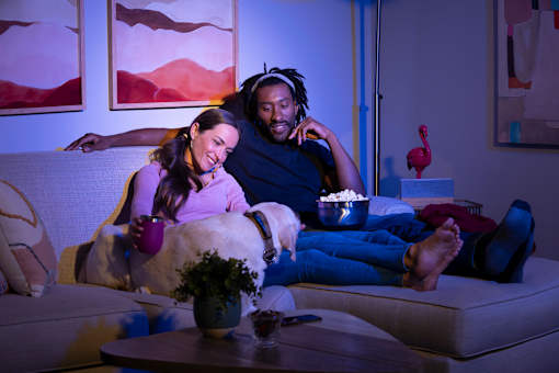 A man and woman are sitting on a couch with a dog between them, both wearing headphones and looking at a tablet.at Copper Creek Apartments, Las Vegas, 89123